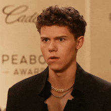 a young man wearing a necklace and a black jacket stands in front of a sign that says peabody award