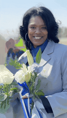 a woman in a suit is holding a bouquet of flowers and smiling