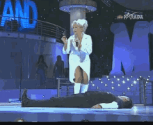 a woman singing into a microphone while a man lays on the stage