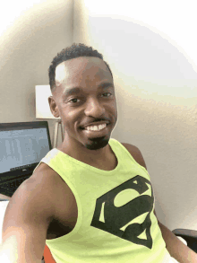 a man wearing a yellow tank top with a black superman logo