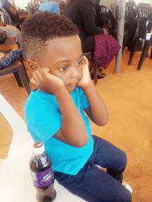 a young boy sits next to a bottle of fanta