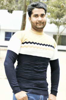 a man wearing a yellow white and blue sweater stands in front of a building