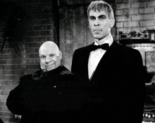 a man in a tuxedo stands next to another man with a bald head