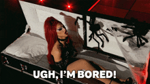 a woman with red hair is laying in a coffin with the words ugh i 'm bored below her