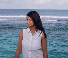 a woman in a white shirt is standing on the beach in front of the ocean .