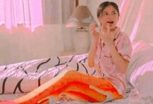 a woman is sitting on a bed wearing a mermaid costume and eating a fish .