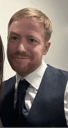 a man with a beard wearing a white shirt and blue vest