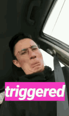 a man sitting in a car with a pink box that says triggered