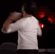 a man in a white shirt is dancing in a dark room with a lamp in the background .