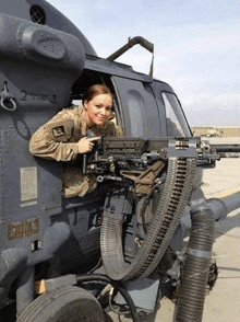 a woman in a military uniform is sitting in the cockpit of a helicopter holding a gun .