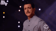 a man with a mustache stands on a stage in front of a sign that says yo soy el maestro