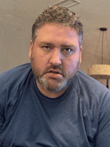 a man with a beard wearing a blue shirt is looking at the camera