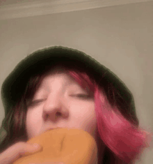 a woman with pink hair wearing a green hat eating a donut