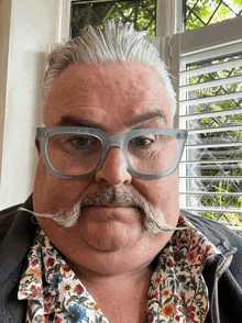 a man with glasses and a mustache is wearing a shirt with flowers