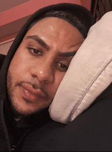 a man in a black hoodie is laying on a bed with his head on a pillow