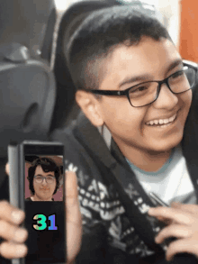 a boy with glasses is holding up a phone with the number 31 on it