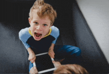 a young boy is sitting on a couch holding a tablet with his mouth open