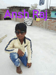 a young boy wearing sunglasses kneeling on a roof with the name ansh raj