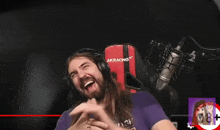 a man wearing headphones and a red akracing chair laughs in front of a microphone