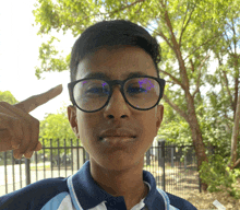 a young man wearing glasses is pointing his finger at his forehead