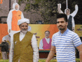 a man in a blue and white striped shirt stands next to a man in a turban in front of a political poster