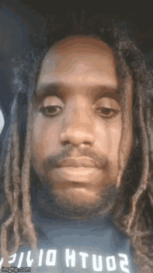 a close up of a man 's face with dreadlocks and a beard wearing a black shirt .