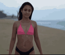 a woman in a pink bikini is standing on the beach