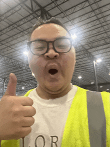 a man wearing glasses and a yellow vest gives a thumbs up sign