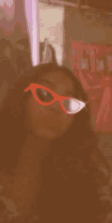 a woman wearing red sunglasses is taking a selfie in front of a pink curtain .