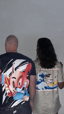 a man and a woman are standing next to each other wearing shirts with a cartoon on the back