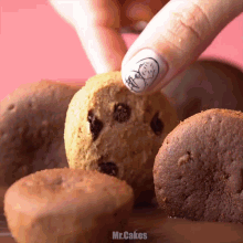 a close up of a person 's hand reaching for a chocolate chip cookie with the words mr.cakes below it