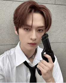 a young man in a white shirt and black tie holds a gun