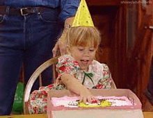 a little girl wearing a party hat is sitting at a table eating a birthday cake .