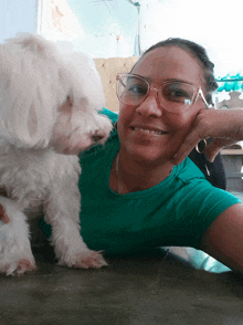 a woman wearing glasses and a green shirt is holding a small white dog