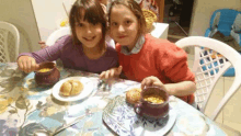 two young girls are sitting at a table eating food