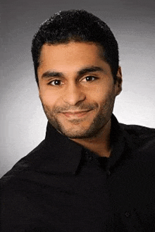 a man with a beard is wearing a black shirt and smiling at the camera .