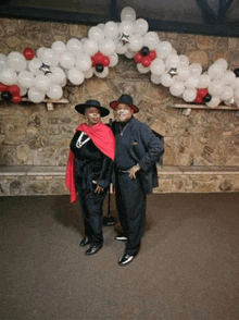 a man and a woman standing in front of a wall of balloons