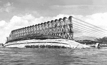 a black and white photo of a bridge in the middle of the water .