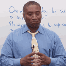 a man in a blue shirt and tie stands in front of a white board with the words one in key to self written on it