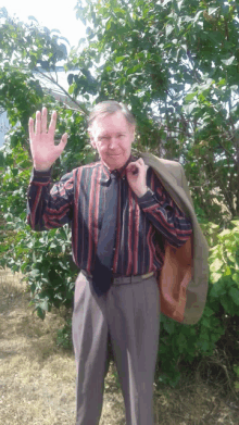 a man in a striped shirt and tie holds his jacket over his shoulder and waves