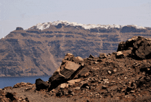 a mountain with snow on top of it is surrounded by rocks and a body of water