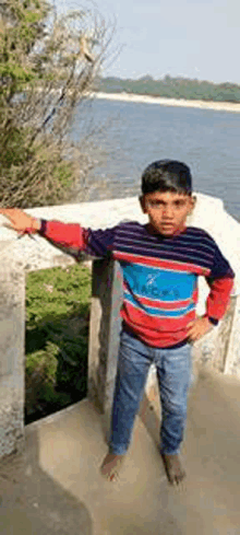 a young boy in a striped shirt is standing next to a railing near a body of water .