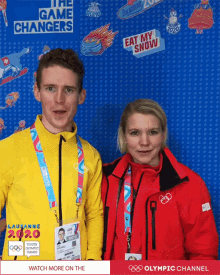 a man and a woman are posing for a photo in front of a wall that says " the game changers "