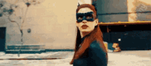 a woman wearing a cat mask and sunglasses is standing on a sidewalk .