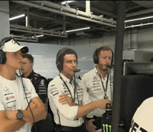 a group of men wearing headphones are standing in front of a computer monitor .