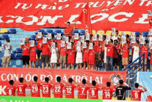 a group of soccer players are standing in front of a large red banner that says con loc do da tro lai .