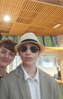 a man wearing sunglasses and a hat stands next to another man wearing a suit