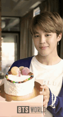 a young man is holding a cake and a box with bts world on it