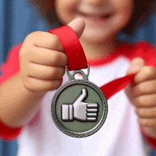 a child is holding up a medal with a thumbs up sign on it