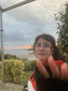 a woman wearing glasses holds up her hand in front of the ocean